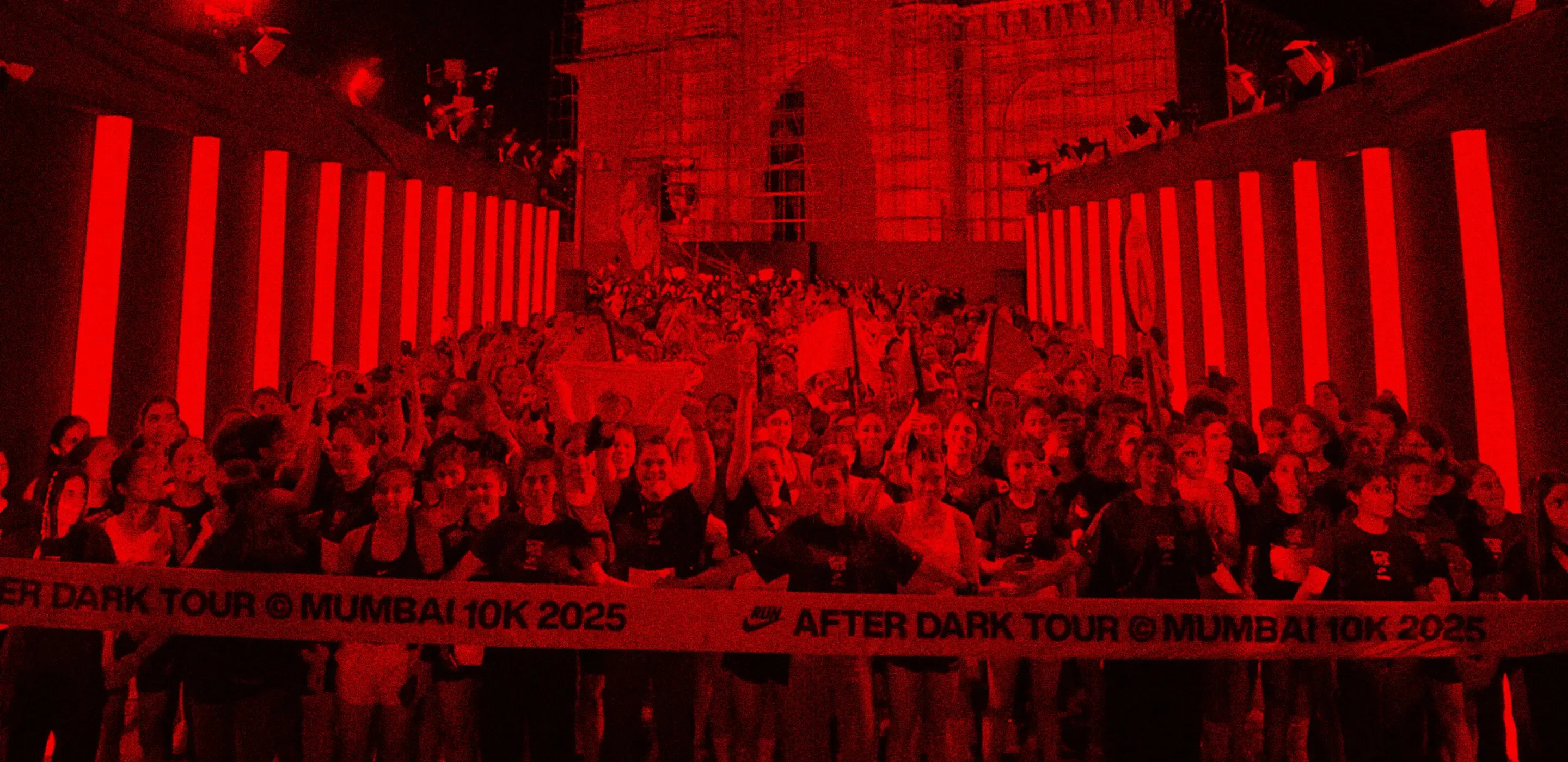 A crowd of runners at the red-lit start line in front of the Gateway of India