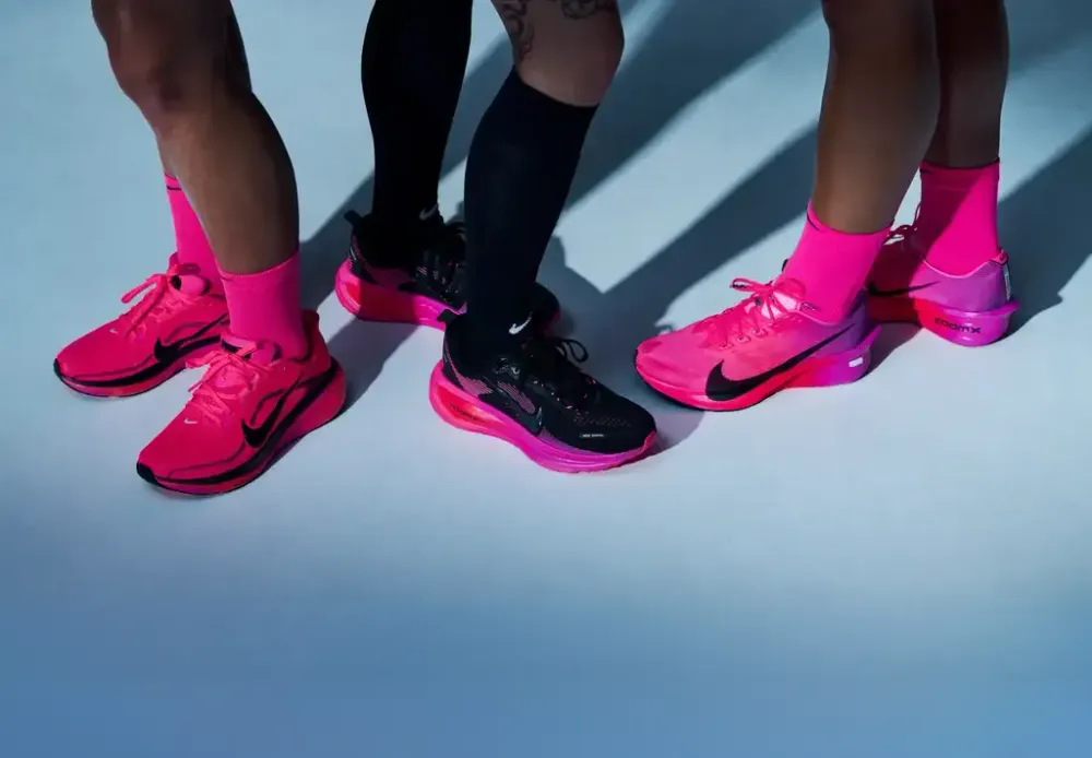 Three runners in pink Nike running shoes on a pale studio floor