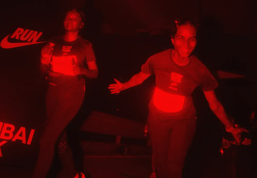 Runners under red light passing a Nike Run Mumbai backdrop