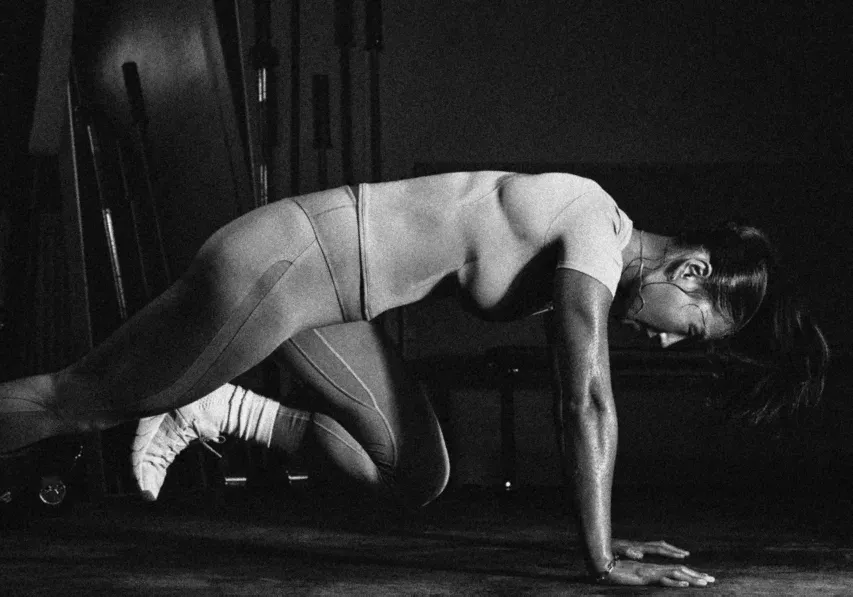 Runner on hands and knees mid-exercise in a dark gym